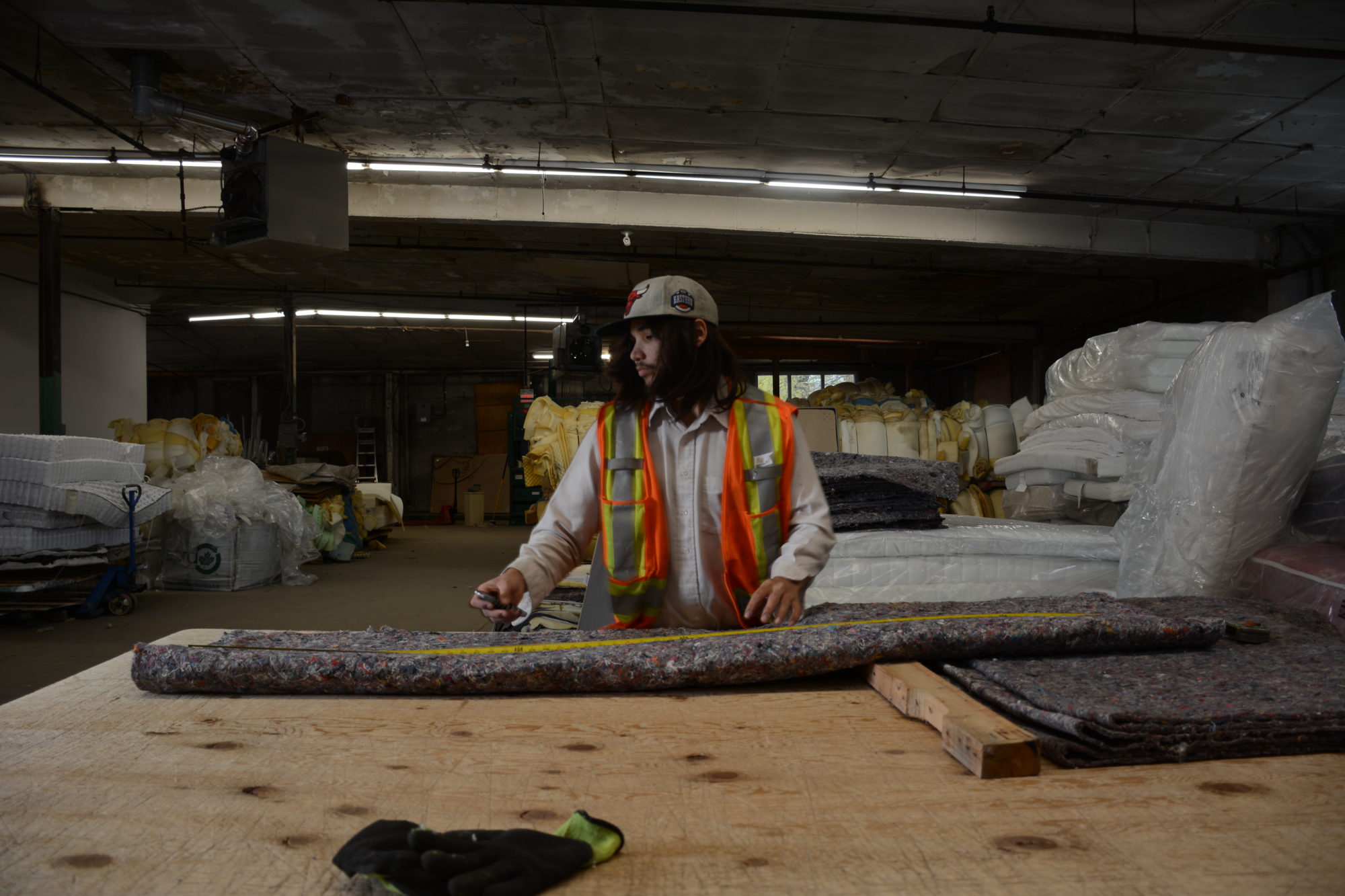 A man in safety PPE attends to a sheet of fabric in a basement warehouse. 