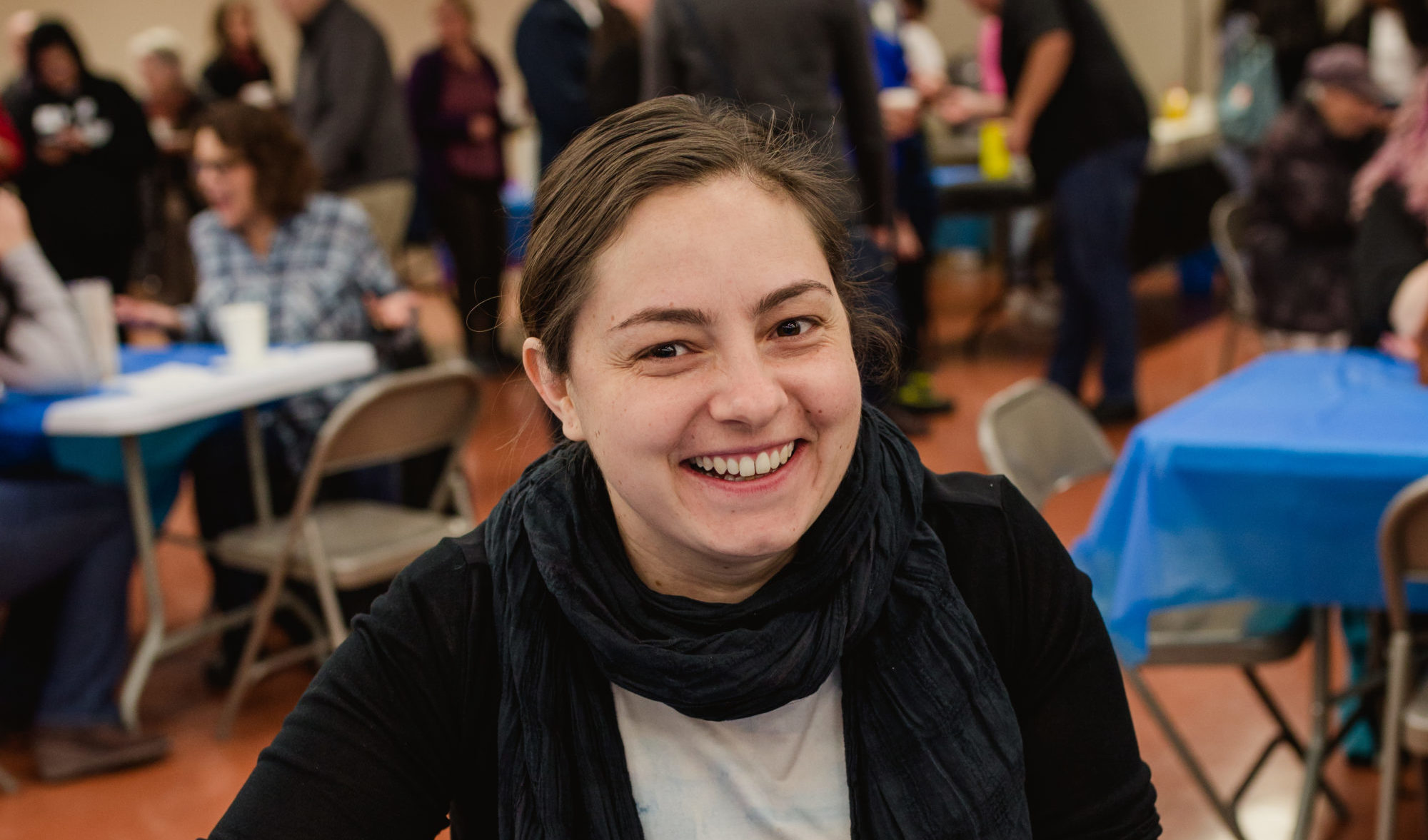 A pancake breakfast, where a woman smiles with her meal while others converse in the background.