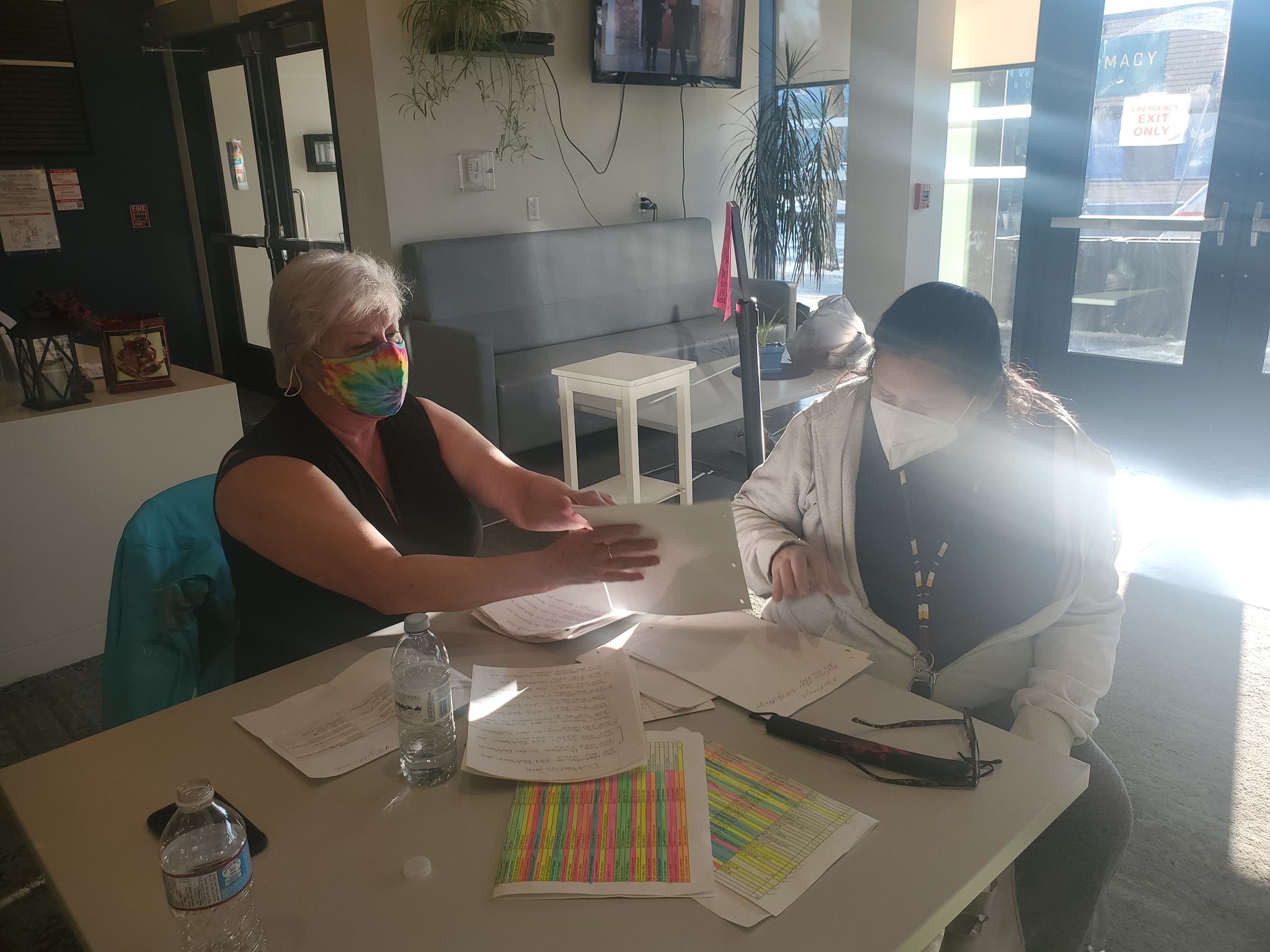 A woman helps another person with papers, sitting at a table.