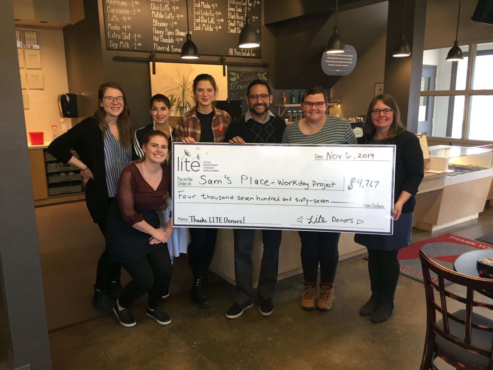 People hold a giant cheque, which shows Sam's Place-Workday Project earned over four thousand dollars from Lite donors. 