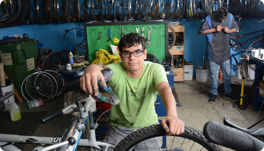 A man holds a tool in his hand over a bike, standing in a garage.
